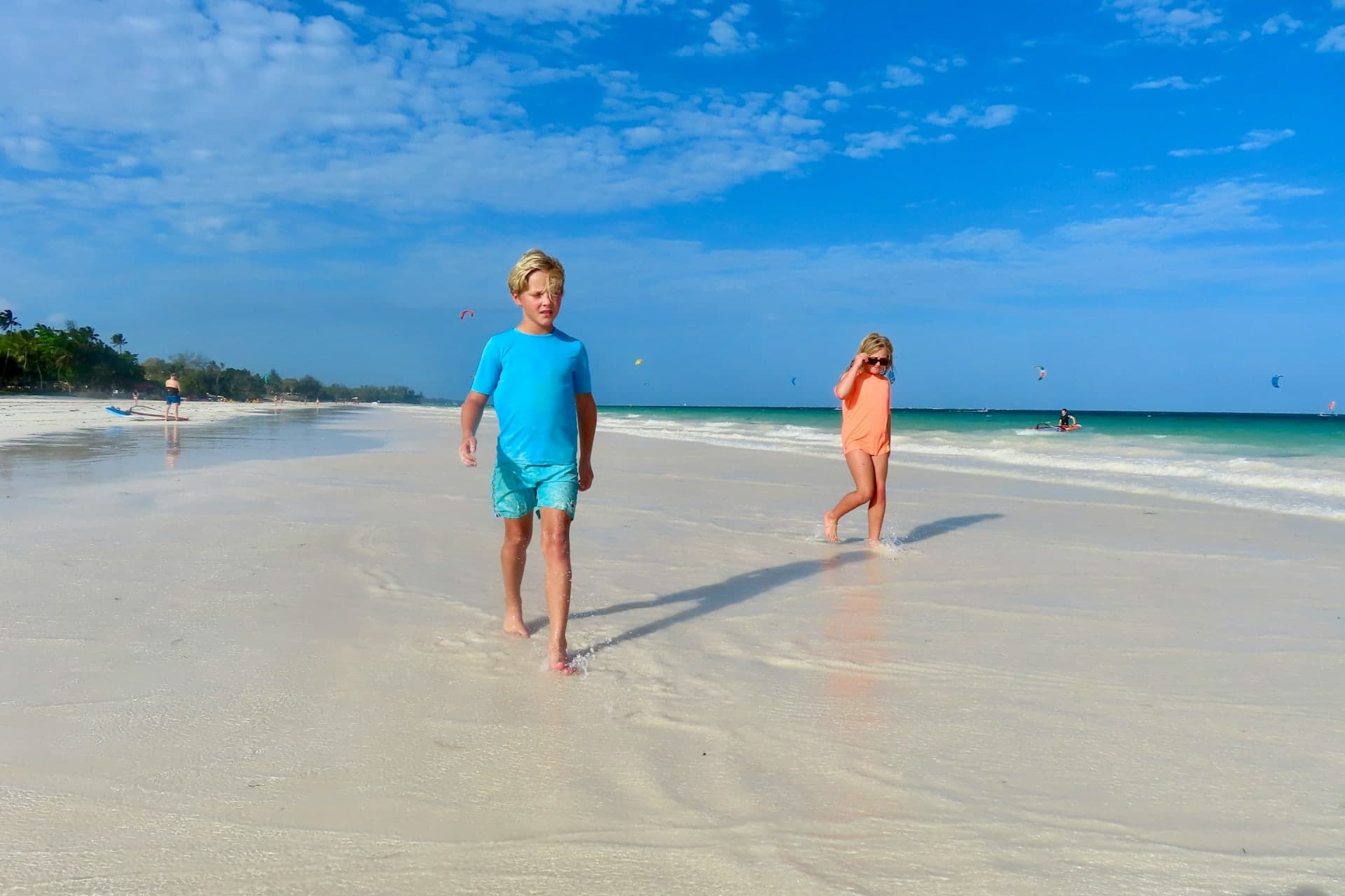 Two children walking on a white sand beach at low tide